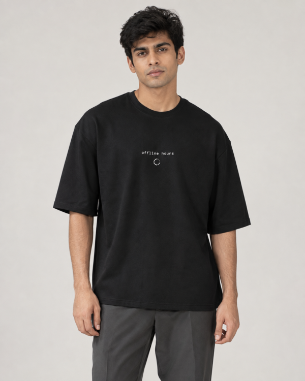 Model wearing a black oversized Toxikiing t-shirt with a small centred chest print reading 'offline hours' in monospace lowercase above a dotted loading-spinner circle